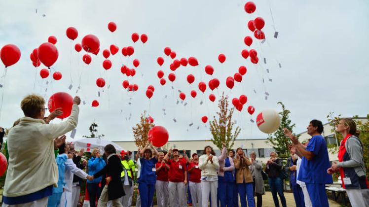 100 Luftballons mit Daumenabdrücken der Mitarbeiter auf Karten steigen in den Himmel.  