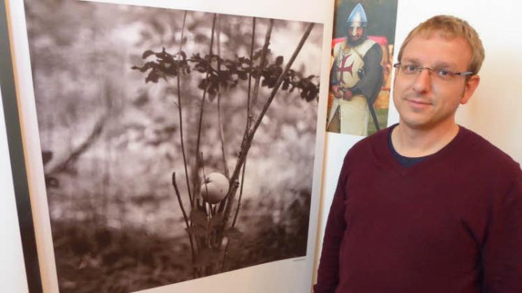 Pastor Christian Lange steht vor einem Apfel-Foto von Roger Schmidt mit dem Titel „Aufgefangen“.  