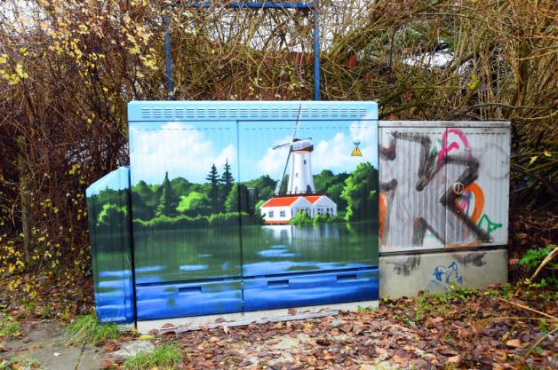 Zweimal Graffiti: In der Neumühler Straße liegen romantische See-Landschaft mit Mühle und graue Schriftzüge direkt nebeneinander.