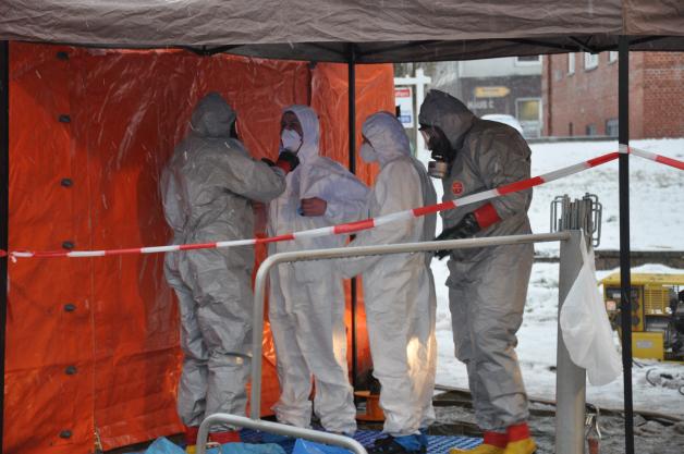 Einsatzkräfte haben zwei Personen in weißen Schutzanzügen zum Dekontaminationszelt gebracht.