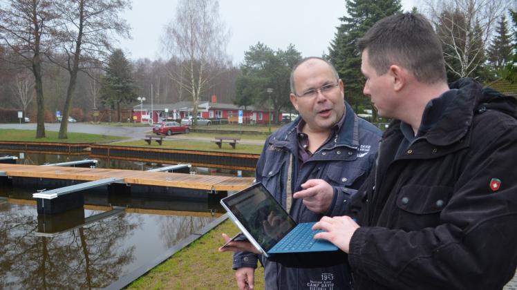 Henry und Oliver Misch (v.l.) sehen sich vor der neuen Bootssteganlage auf einem Laptop den neuen Internet-Auftritt des Campingplatzes an. 