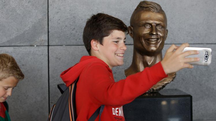 Ein Junge macht am Flughafen in Funchal ein Selfie mit der Büste von Fußballer Cristiano Ronaldo von Real Madrid. 