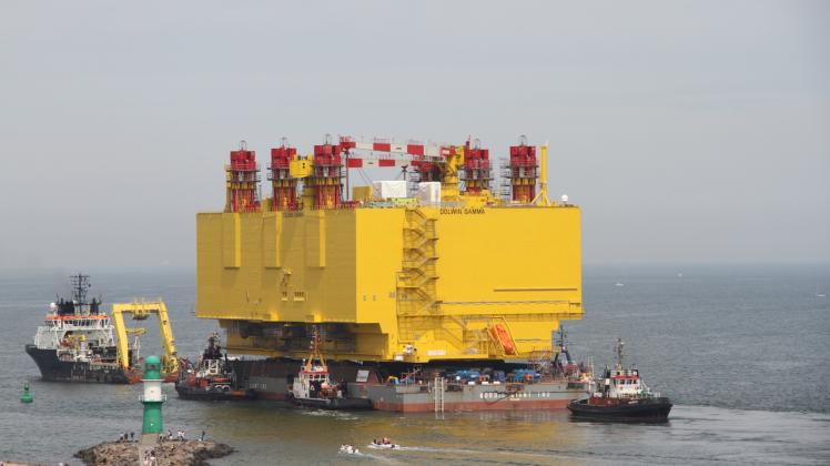 Eskortiert von Schleppern verlässt die Offshore-Plattform DolWin Gamma die Werft und Warnemünde. Das Molenfeuer der Ostmole wirkt da wie ein Winzling. 