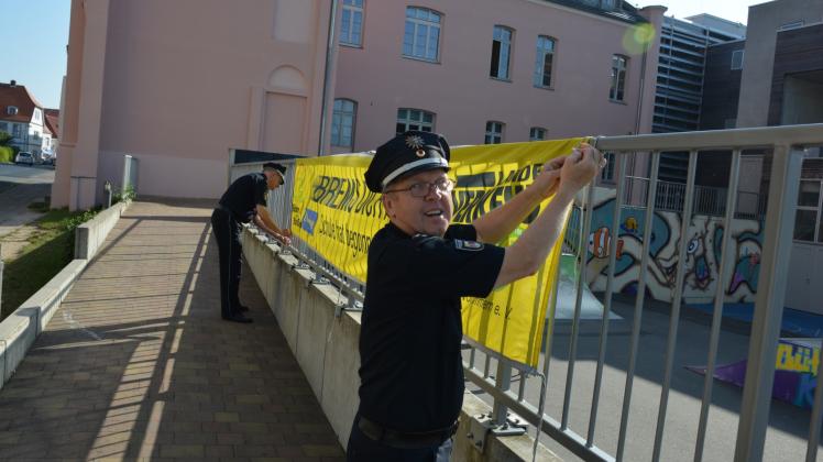 Sie setzen wieder ein Zeichen: Kontaktbeamter Uwe Wiencke (r.) und Revierleiter Dirk Höhlein brachten gestern das gelbe Banner vor der Schule am Schlossplatz an.   