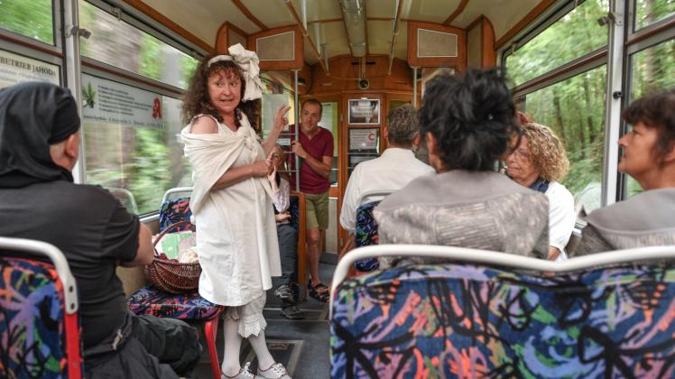 Stadtführerin Katrin Fleischer steht im Kostüm als „Katharina – die Wäscherin vom Kalksee“ in einer fahrenden historischen Straßenbahn Baujahr 1959/61 und erzählt einer Besuchergruppe etwas zur Geschichte des Ortes Woltersdorf. 