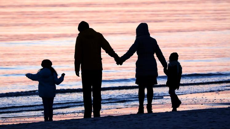 Eine Familie ist im Licht der untergehenden Sonne an der Ostsee auf der Insel Hiddensee bei Vitte unterwegs.