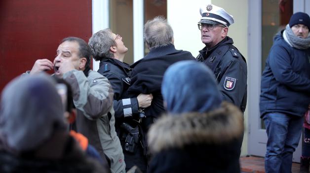 „Stadtbekannter Querulant“: Ein Mann wird nach seiner Stock-Attacke gegen Demonstranten von Polizisten in ein Café geführt. 