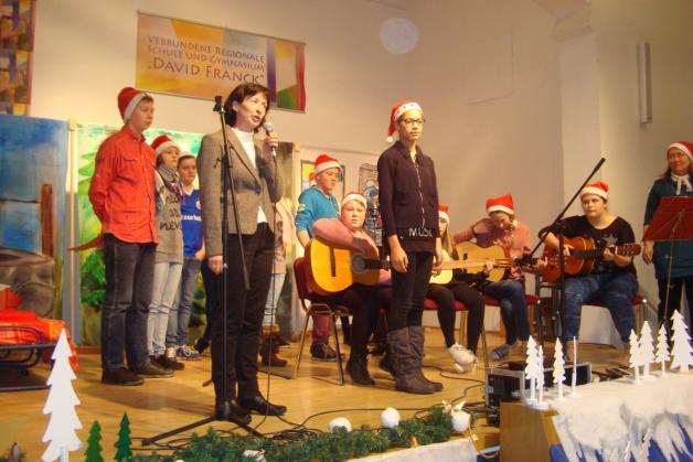 Schulleiterin Annett Laß eröffnet das Programm und begrüßt die Gäste, Sabine Schürer (re.) übte den 1. Teil mit den Kindern ein, mit vier Gitarren und Melodica. 