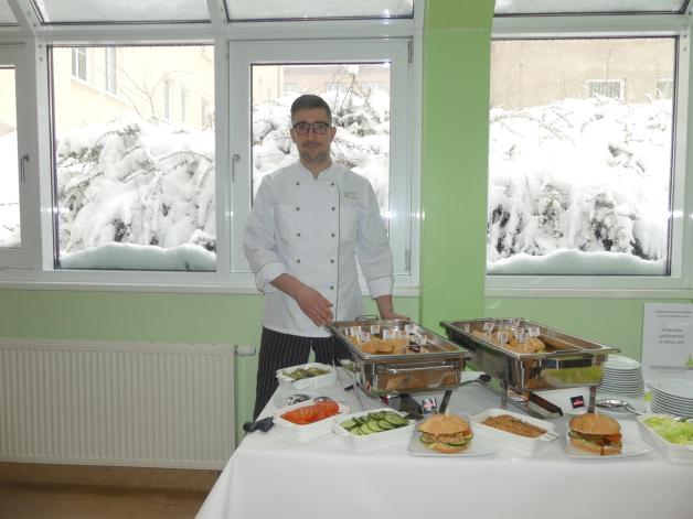 Ganz frisch zubereitet präsentiert Mensa-Koch Christoph Maykopf den Verkostern den Jubiläumstaler mit Salat, Tomate, Gurke, Röstzwiebeln und Curry-Soße als Burger. 