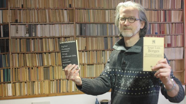 Der Warnemünder Buchhändler Frank Weisleder vor der Sammlung mit seinen 1380 Büchern aus der Reclam-Universalbibliothek. In der Hand hat er zwei seiner Lieblingsbücher der Reihe. 