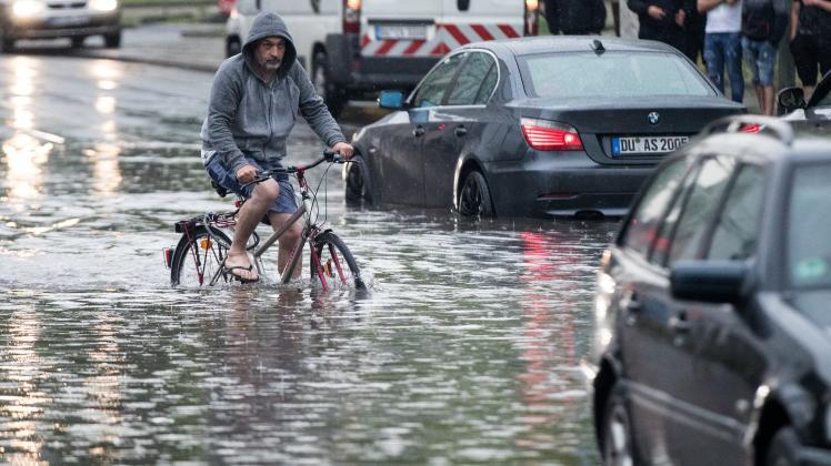 Ein Radfahrer fährt über eine überflutete Straße an liegengebliebenen Autos vorbei.
