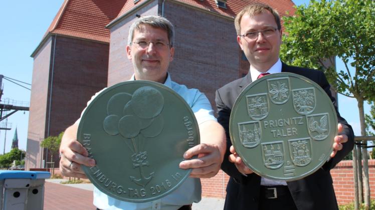 So groß ist der Original-Taler nicht: Wittenberges Bürgermeister Oliver Hermann (l.) und André Wormstädt von der Sparkasse Prignitz zeigen die beiden Seiten der Münze.