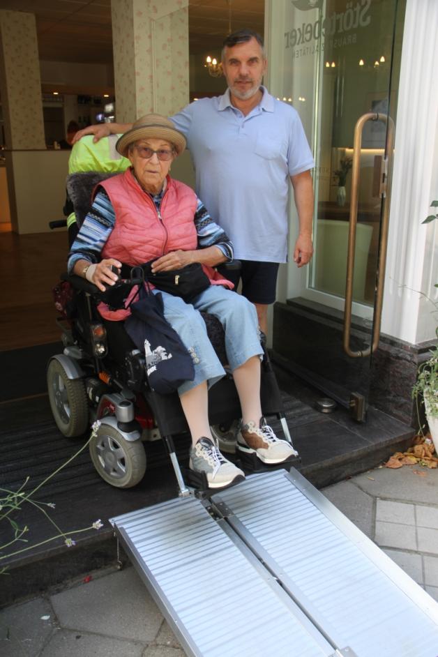 Hat eine Alu-Rampe angeschafft, damit die Gäste mit Rollstühlen oder Rollatoren ins Café kommen können. Gastronom Olaf Weber mit Rollstuhlfahrerin Margarete Eichler. „Das ist prima“, lobt sie.