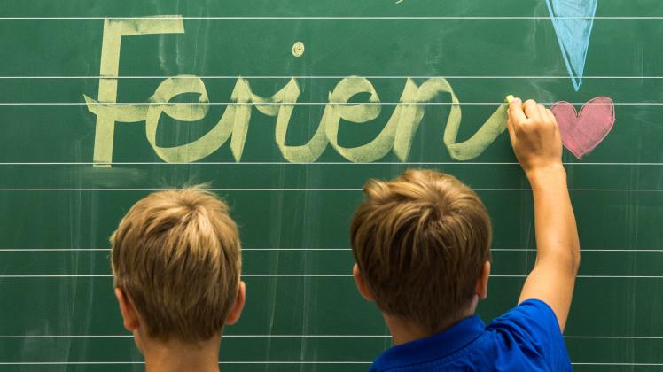 Drittklässler einer Grundschule schreiben am Dienstag «Schöne Ferien!» auf eine Tafel in einem Klassenzimmer.