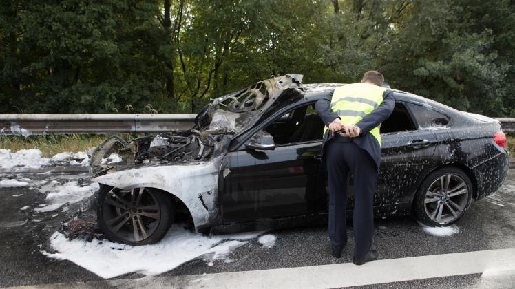 Der Fahrer begutachtet das ausgebrannte Wrack seines BMW.