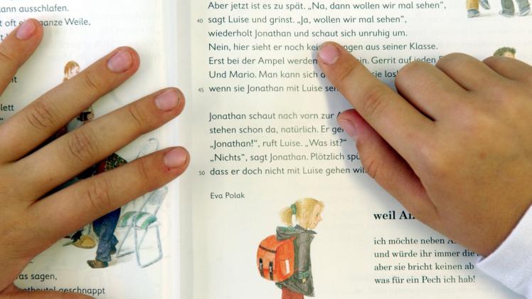 Buchstabe für Buchstabe gleiten die Finger eines Jungen über die Seiten eines Buches. Ab dem kommenden Schuljahr wird in den 1. Klassen wieder nach der Fibel-Methode gelernt.