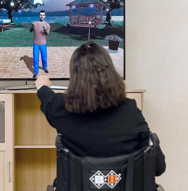 Therapie: Eine  Pflegeheim-Bewohnerin bewegt Hände und – so gut es eben geht – auch Füße, genauso wie der computeranimierte Vortänzer auf dem großen Bildschirm.