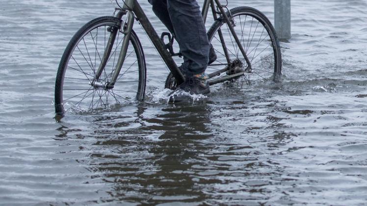 Ein Radfahrer fährt durch eine überflutete Straßenkreuzung in Wismar.