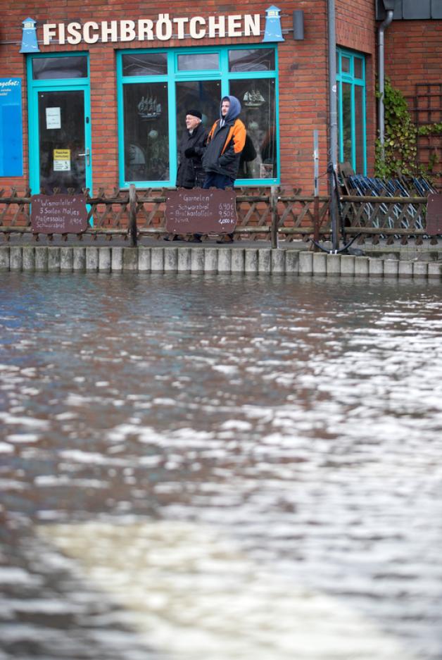 Zwei Männer beobachten vor einem geschlossenen Fischladen im Stadthafen von Wismar das Ansteigen des Hochwassers. 