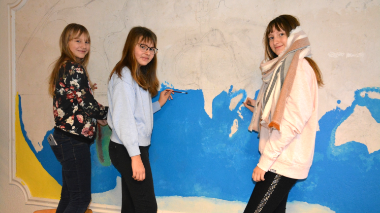 Um das Foyer ihrer Schule zu verschönern, gestalten die Schülerinnen Melina, Elisa und Mairin (v.l.) gemeinsam eine große Weltkarte.