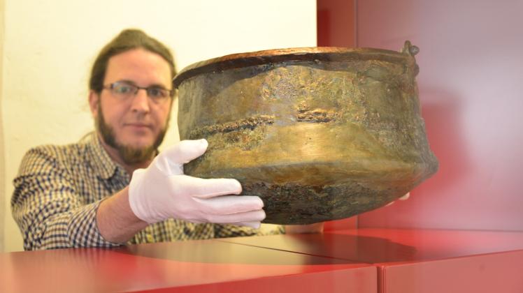 Sieht unspektakulär aus, hat es aber in sich: Der wissenschaftliche Museumsmitarbeiter Thomas Kühn platziert die fast 2000 Jahre alte Bronzeurne, die 1995 in Hagenow gefunden wurde, an ihrem Ausstellungsplatz in der neuen Dauerausstellung. 