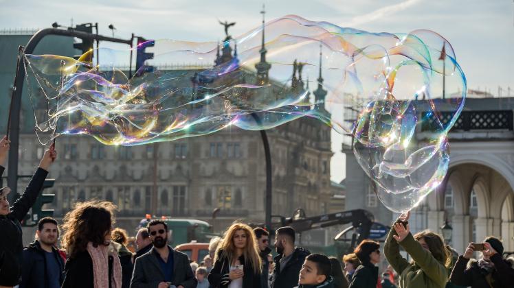 Ein Straßenkünstler lässt im strahlenden Sonnenschein vor dem Hamburger Rathaus Seifenblasen in die Luft steigen. 