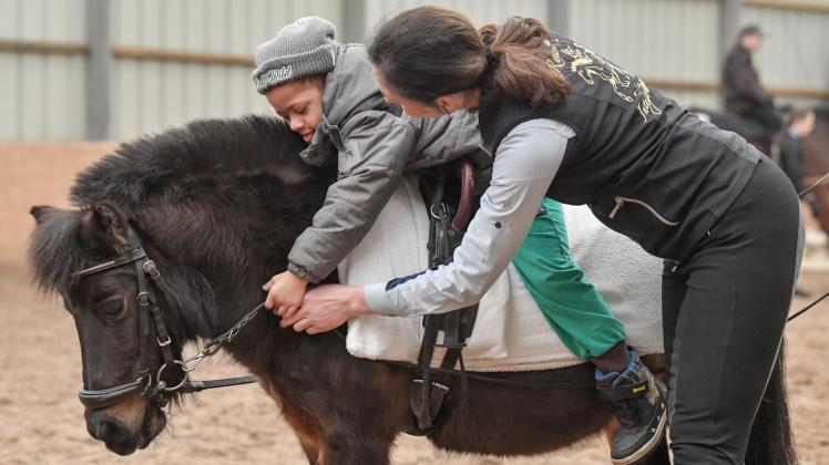 Andrea Harwardt, Vorsitzende vom Reitverein Integration  unterstützt Jamil, ein Kind mit Down-Syndrom, beim Reiten auf dem Shetlandpony Cleo. 
