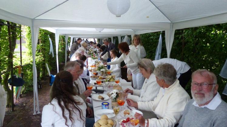 Die Gäste des „Weißen Dinners“ nehmen an einer weiß eingedeckten Tafel im Laubengang des Schlossgartens Platz. 