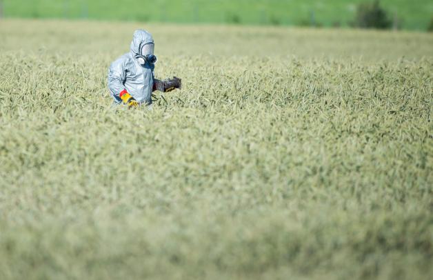 Ein Mitarbeiter der Flugsicherheit der Bundeswehr mit einem Schutzanzug trägt ein Trümmerteil auf einem Feld. 