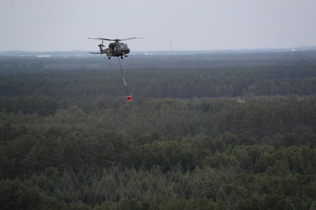 Ein Hubschrauber der Bundeswehr vom Typ NH90 mit einem Löschwasser-Behälter fliegt über einem Wald in der Nähe von Lübtheen. 