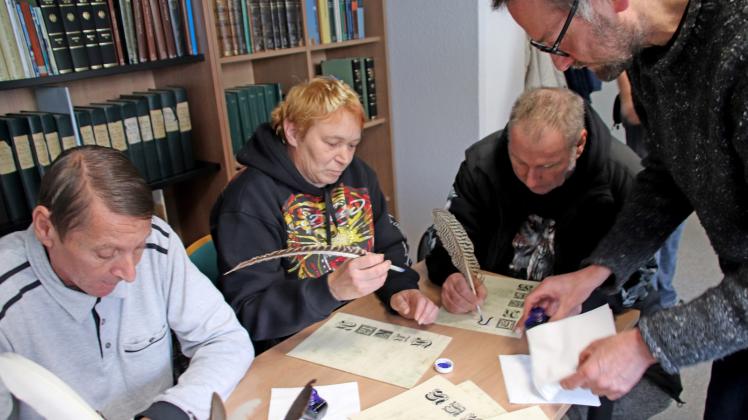 Sie probieren sich im Stadtarchiv Wismar mit dem Schreiben mit einer Gänsefeder aus: Bernd Hein, Kriemhild Ruß und Roland Hunds (v.l.) Dirk Einbeck (r.) rettet mit Servietten den Tisch vor Tintenflecken. 