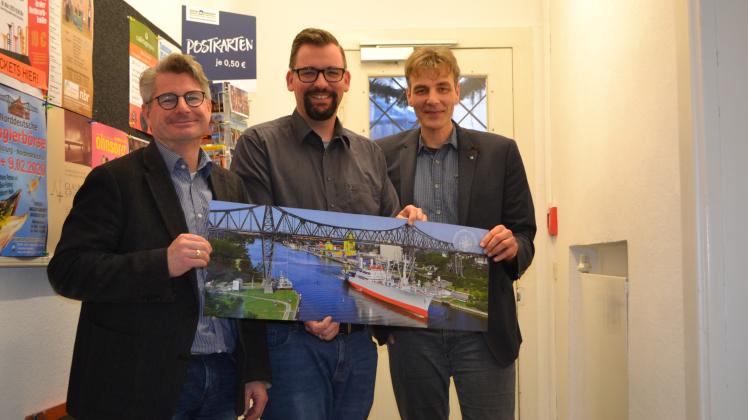 Ein Foto der Rendsburger Hochbrücke ist auf dem neuen Prospekt zu sehen. Es wird präsentiert von Andreas Betz, Heiko Müller und Marco Neumann (von links).