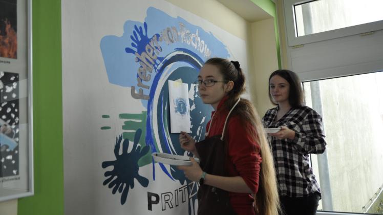 Eileen (links) und Alexandra, Schülerinnen der 10. Klasse, malen das Rochow-Schul-Logo an die Wand im Schulflur. 