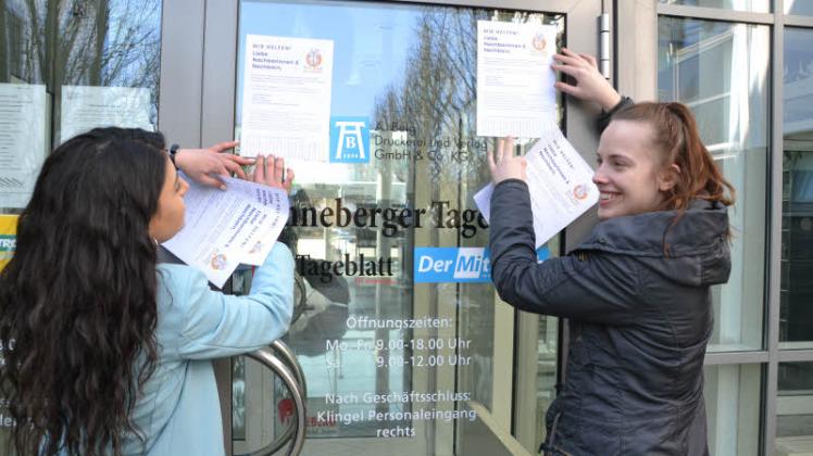 Karina Vartanjan (links) und unsere Auszubildende Kim Treiber bringen Flyer an unserem Verlagsgebäude in Pinneberg an. Ziel ist es, Hilfesuchende und Helfer im Kreis Pinneberg zu vernetzen.