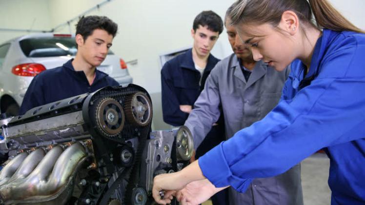 Am Vebrennungsmotor erhält eine Auszubildende zur Kfz-Mechatronikerin in der Werkstatt fachkundige Anleitung.