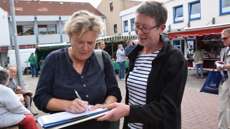 „Auf jeden Fall“ solle der Wochenmarkt dort bleiben, wo er ist – findet die Arnisserin Elke Horn (li.) und setzt zur Bestätigung ihre Unterschrift auf Sigrid Lorenzens Liste.