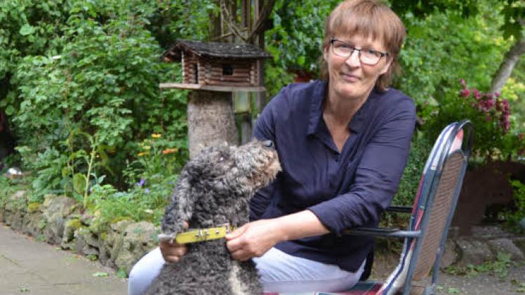 Kirsten Kühl sitzt mit Königspudel-Dame Mia im Garten, der auch das Bauernhof-Café bildet. Sie ist seit der Kommunalwahl 2018 Vorsitzende des Sozial- und Kulturausschusses in Lutzhorn. 