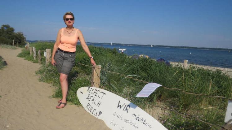 Sabine Mues, Bürgermeisterin in Noer, vor einem Surfbrett, das auf die geltenden Regeln hinweist.
