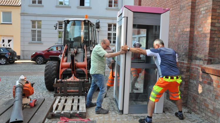 Gemeinsam angepackt: Mitarbeiter vom Bauhof und der Tourist-Info rücken die Bücher-Telefonzelle zurecht.  