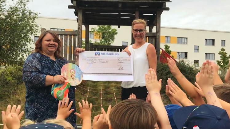 Ein Scheck und viele Kinderhände: Birgitt Lüttjohann (r.) von der VR-Bank übergab die Spende an Kita-Leiterin Ines Kohne. 
