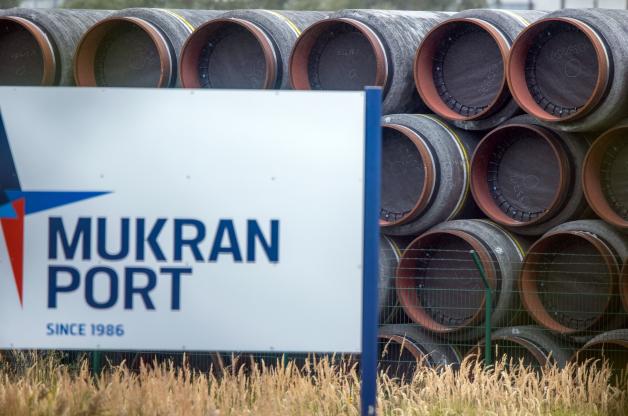 Rohre für die Erdgaspipeline Nord Stream 2 liegen hinter einem Schild mit der Aufschrift "Mukran Port" auf einem Lagerplatz im Hafen Mukran auf der Insel Rügen.