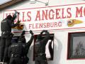 Vermummte Polizisten machen sich mit Akkuschraubern ans Schild am Vereinsheim der „Hells Angels“ in Flensburg.