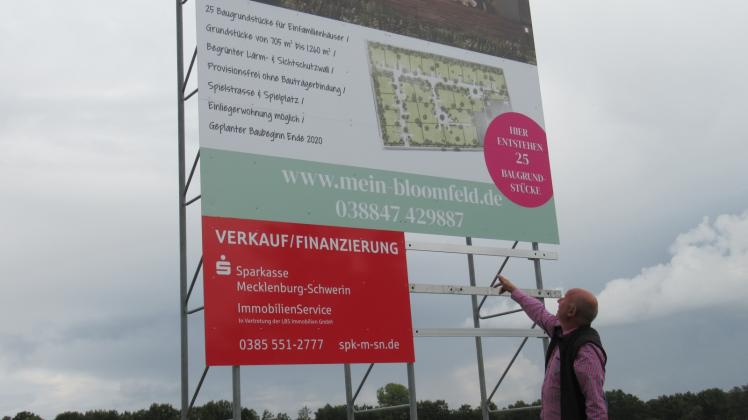 Auf dem Schild werden die Pläne auf der ehemaligen Flohmarktwiese erläutert. Bürgermeister Frank Ahlers freut sich, dass es mit dem Bauen bald losgeht.
