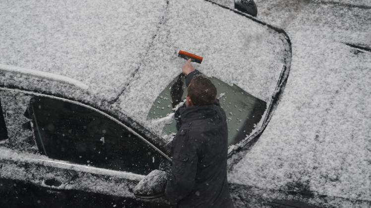 Ein Mann befreit in Hamburg die Windschutzscheibe seines Fahrzeugs vom Neuschnee.