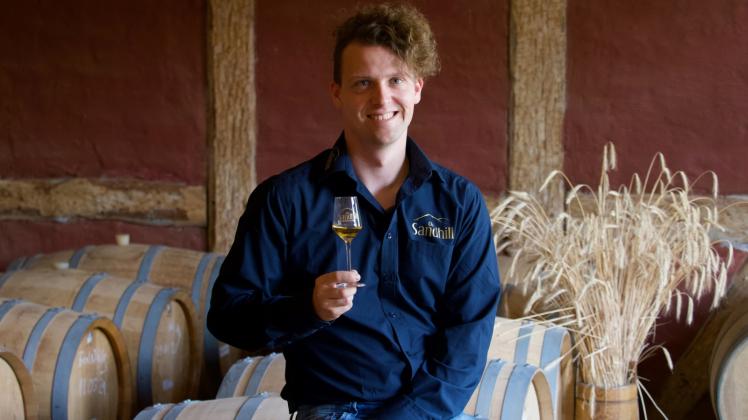 Tim Eggenstein aus Bad Belzig sitzt in seiner Whisky- und Edelbrandmanufaktur vor einem Strauß Gerste – in der Hand hält er ein Glas „Old Sandhill“-Whisky. 