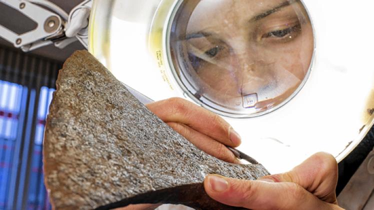 Mit Hilfe einer beleuchteten Lupe reinigt Jamina Hirschberg in der Werkstatt des provisorischen Depots der Landesarchäologen eine Axt aus der Wikingerzeit. dpa