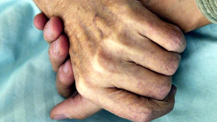 Ein Bild mit Symbolkraft: Ein Sterbebegleiter hält die Hand eines todkranken Menschen. dpa