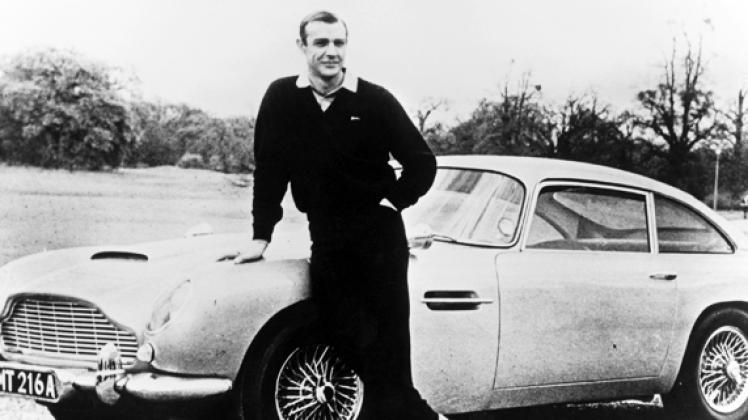 Ein Mann und sein Auto: James Bond (Sean Connery) posiert vor dem Aston Martin DB5. Den Filmagenten im Dienste Ihrer Majestät verbindet eine enge Beziehung zu der britischen Marke.dpa