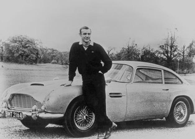 Ein Mann und sein Auto: James Bond (Sean Connery) posiert vor dem Aston Martin DB5. Den Filmagenten im Dienste Ihrer Majestät verbindet eine enge Beziehung zu der britischen Marke.dpa