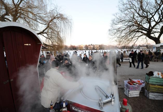 Dampfender Glühwein lockt am Freitag an einem Verkaufsstand am Rand der zugefrorenen Hamburger Außenalster die Kunden an. Foto: Christian Charisius dpa
